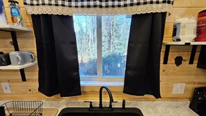 A kitchen with a black sink, a window with a checkered curtain, and a wooden wall.