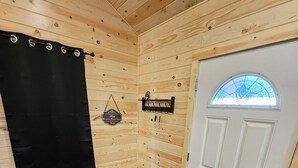 A cozy cabin room with wooden walls, a bench, a door with a window, and a wall-mounted coat rack.
