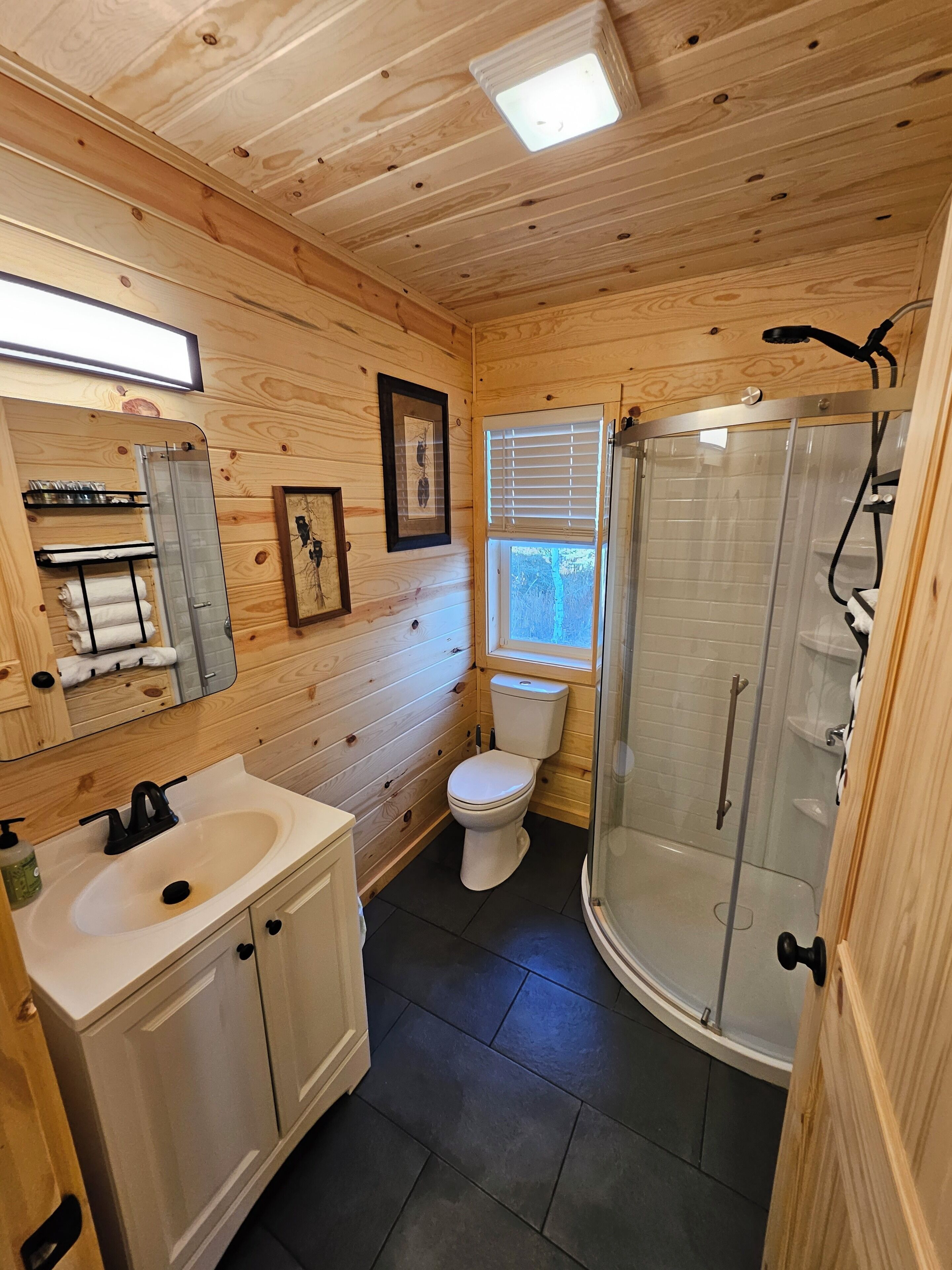 A wooden-paneled bathroom with a sink, toilet, and glass-enclosed shower.