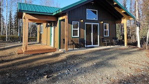 A cabin with a wooden exterior, a green roof, and a covered porch with chairs.