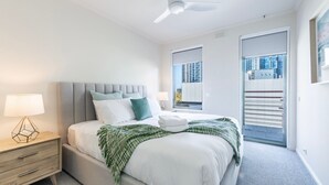 A modern hotel room with a bed, bedside lamps, a view of the city through the window, and a balcony with a railing. - Vista on Queensbridge - 3BR Home in the Heart of It All (Southbank)