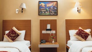 Ein Hotelzimmer mit zwei Betten, einem Nachttisch mit Lampe, einem Bergpanorama und einem kleinen Tisch mit Vase und Telefon.