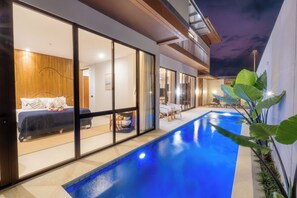 Ein modernes Haus mit Schwimmbad, großen Schiebetüren und einem Balkon.