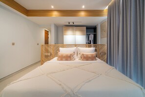 Ein modernes Schlafzimmer mit einem großen Bett, einem Holz-Kopfteil und einem begehbaren Kleiderschrank mit Spiegel und Kleidung.