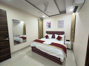 A hotel room with a bed, a ceiling fan, a mirror, and a nightstand. - The Velvet Stay (Jaipur)