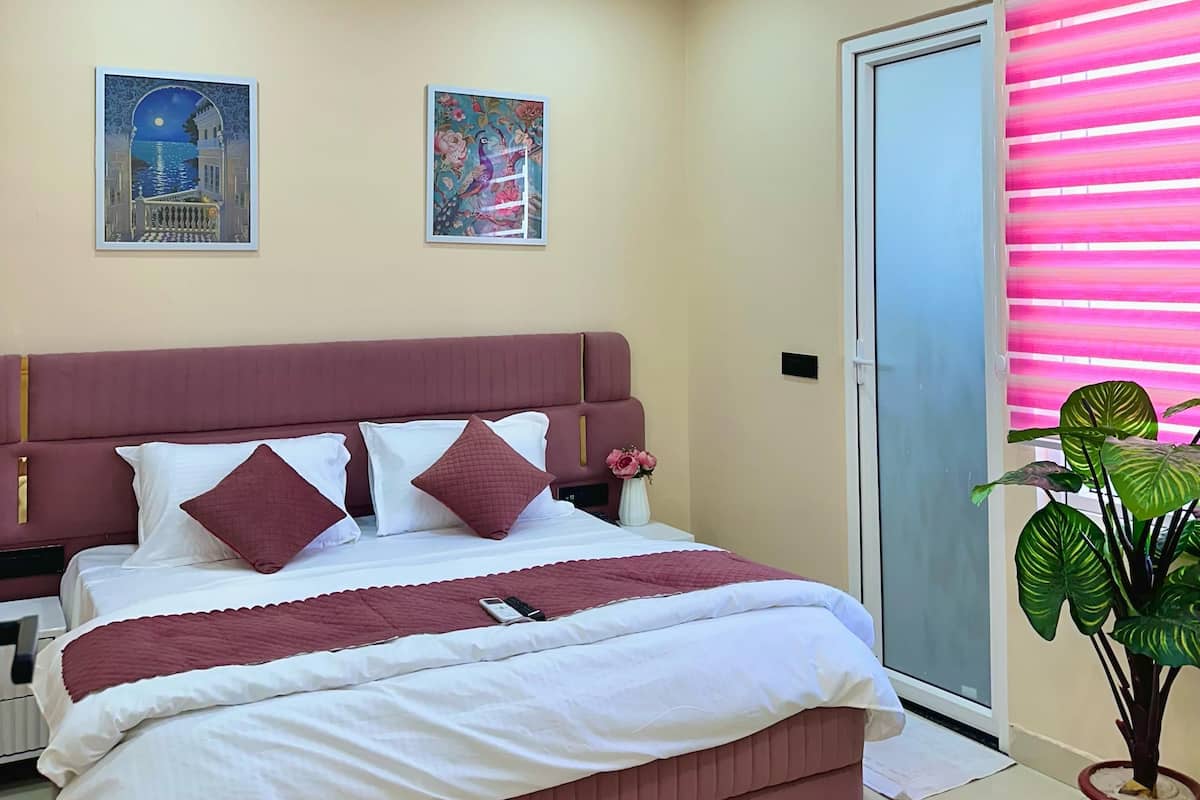 A bedroom with a large bed, two nightstands, a potted plant, and artwork on the walls.