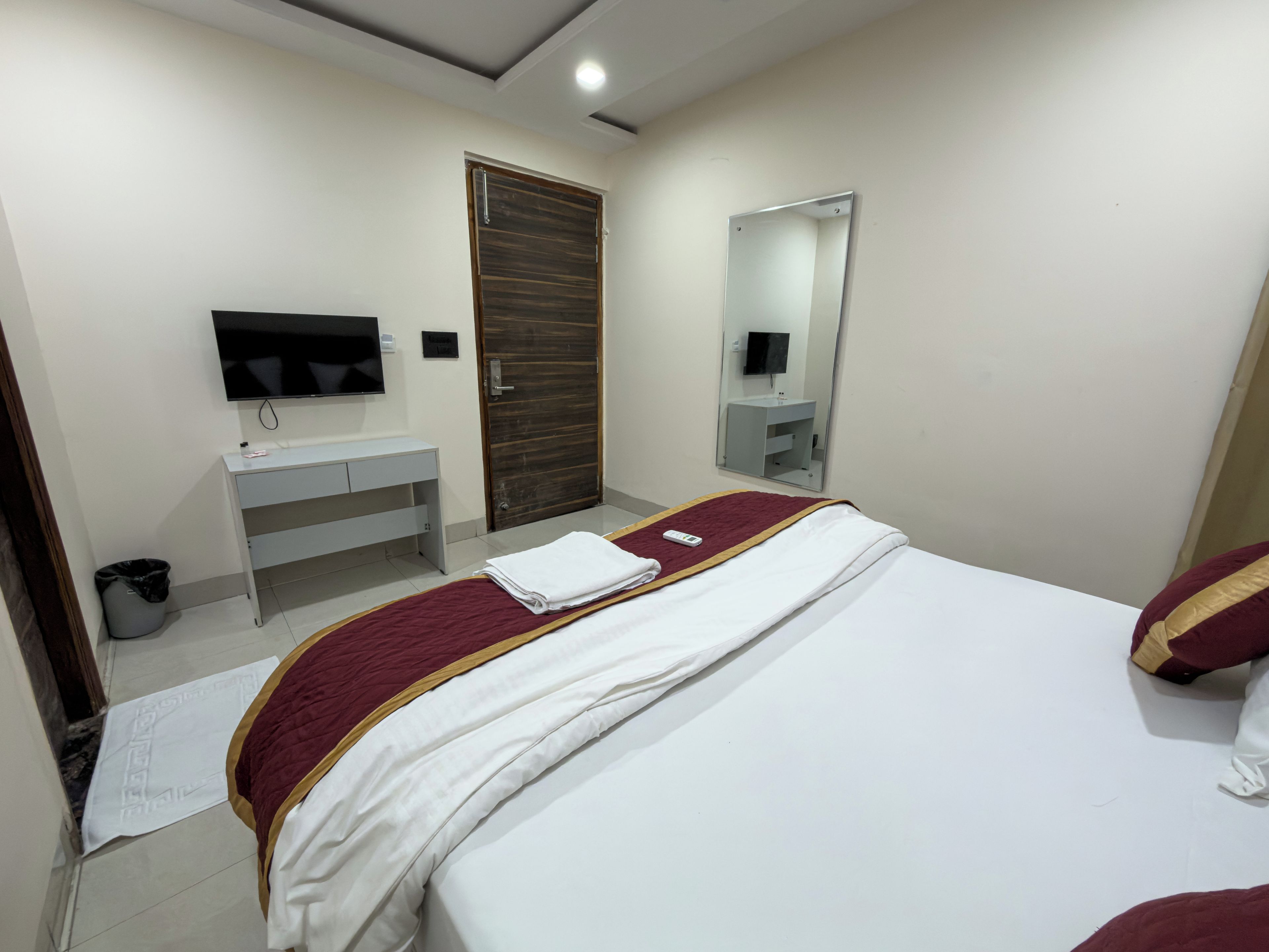 Ein Hotelzimmer mit Bett, Fernseher, Spiegel, Nachttisch und Tür.