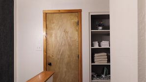 Un corridoio stretto con una porta in legno alla fine, una piccola mensola con asciugamani piegati e una parete bianca.