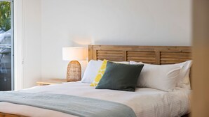 Un lit bien fait, avec une tête de lit en bois, une lampe de chevet et une vue sur l’extérieur grâce à une porte vitrée.