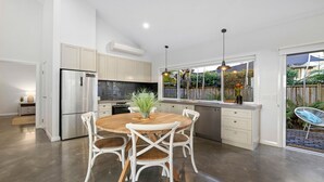 Une cuisine moderne avec des meubles blancs, un réfrigérateur en acier inoxydable et un coin repas comprenant une table en bois et des chaises blanches.