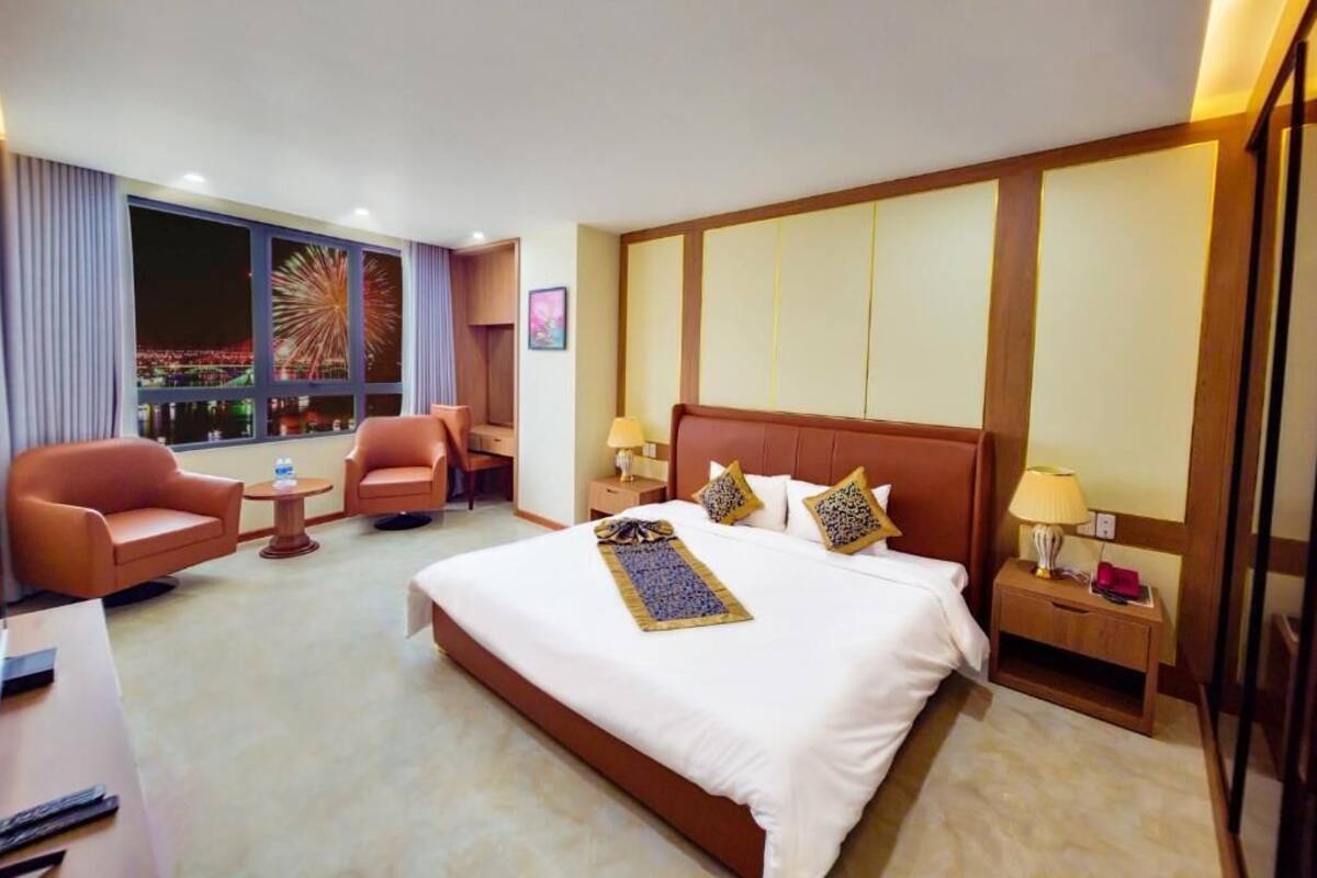 A hotel room with a large bed, two armchairs, a small table, and a nightstand with lamps.