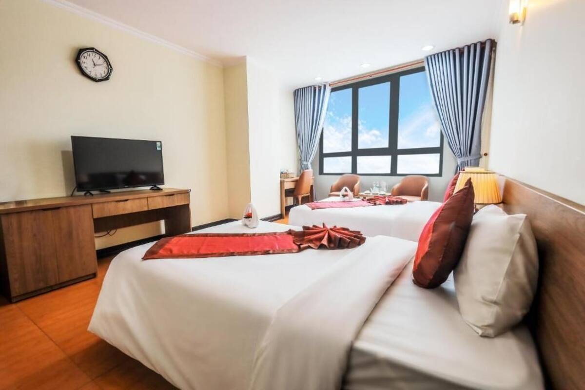 A hotel room with two beds, a desk with a television, a clock on the wall, and a window with curtains.