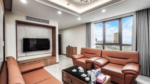 A modern living room with a large flat-screen TV mounted on a marble wall, a brown leather sofa, a matching armchair, and a coffee table with various items. - T.26 Hotel (Da Nang)
