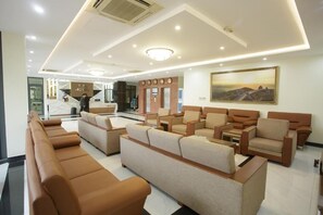 A hotel lobby with a reception desk, seating area with sofas and armchairs, and a large painting on the wall. - T.26 Hotel (Da Nang)