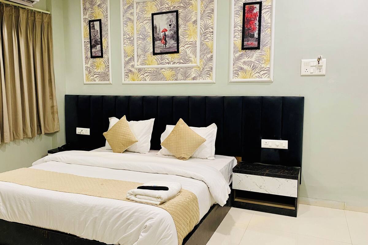A neatly made bed with white and beige bedding, a black headboard, and a bedside table with a black lamp.