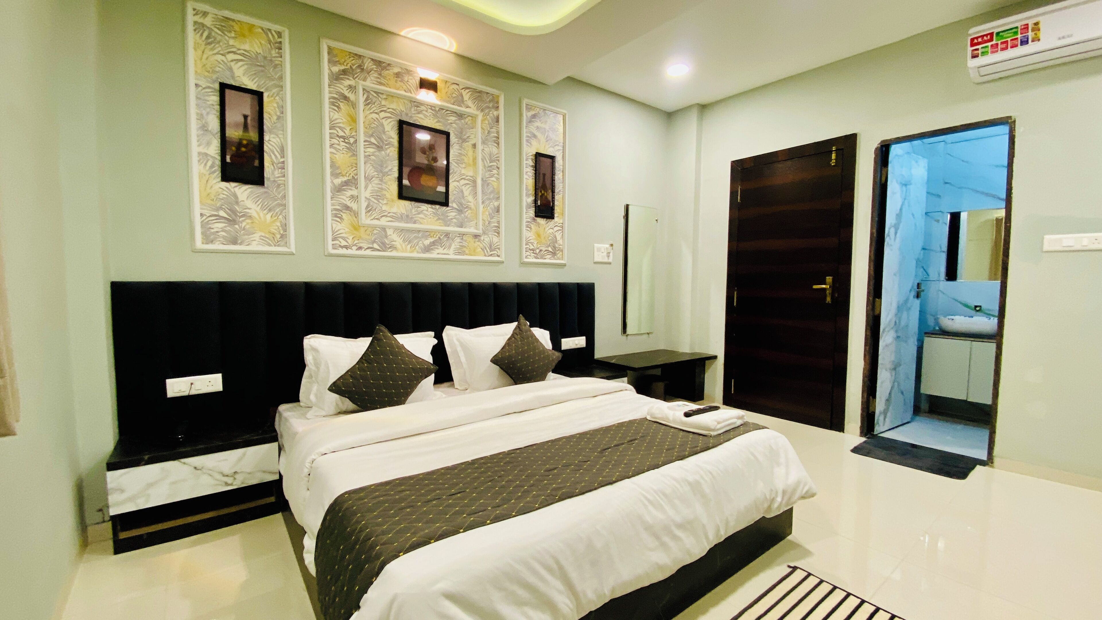 A modern hotel room with a large bed, a nightstand, a mirror, and a bathroom visible through an open door.