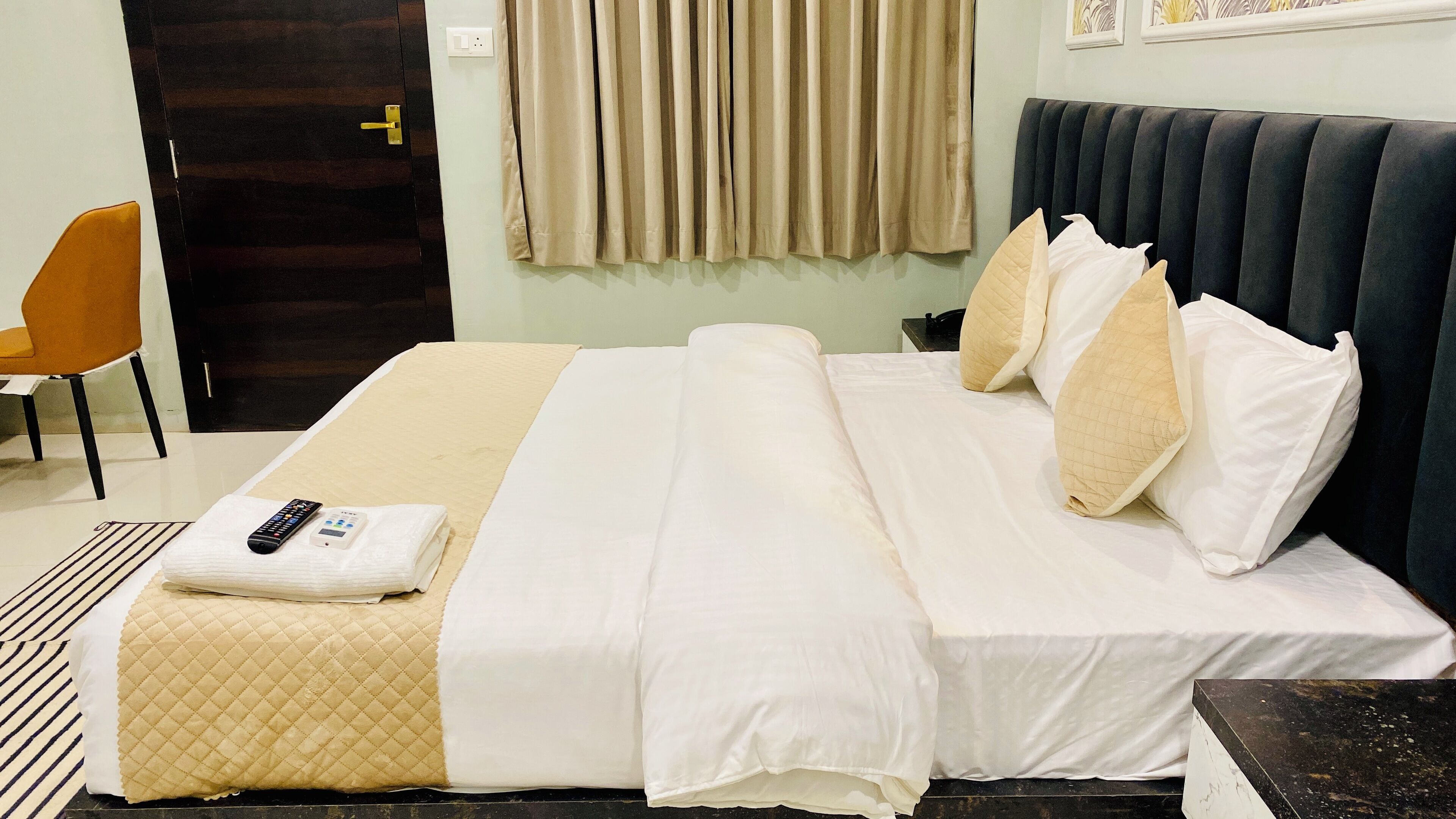 A hotel room with a bed, a chair, a bedside table, and a window with curtains.