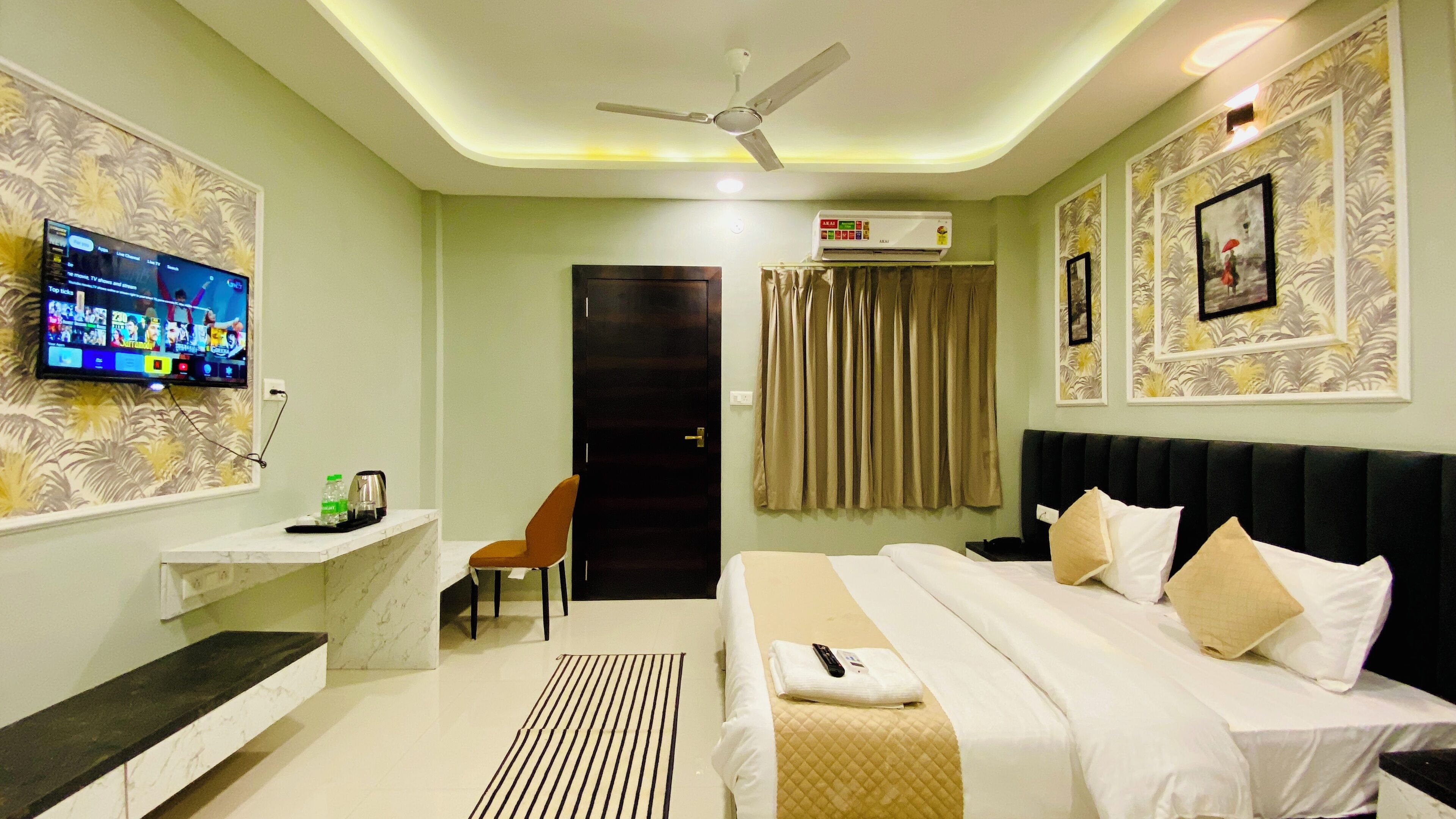 A hotel room with a bed, a TV mounted on the wall, a ceiling fan, and an air conditioning unit.