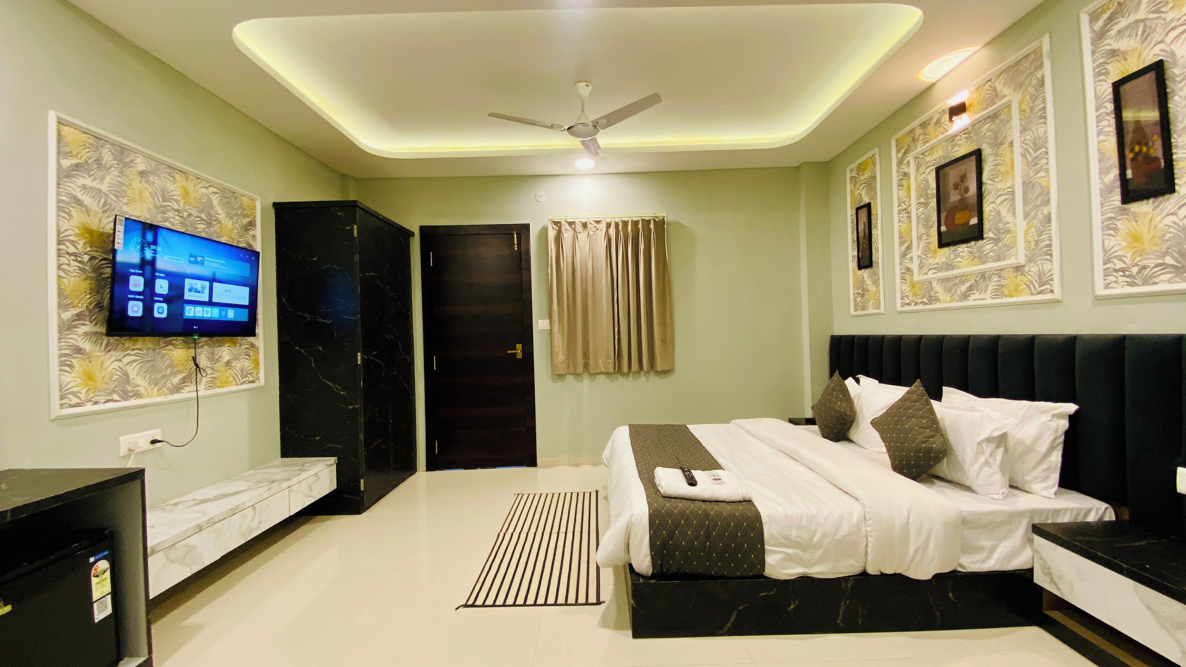 A modern hotel room with a large bed, a flat-screen TV, a ceiling fan, and a minibar.