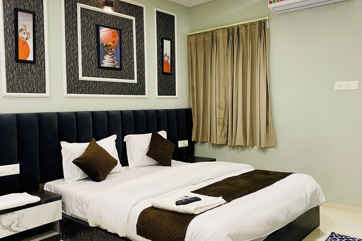 A neatly made bed with white and brown bedding, a remote control, and a marble bedside table.