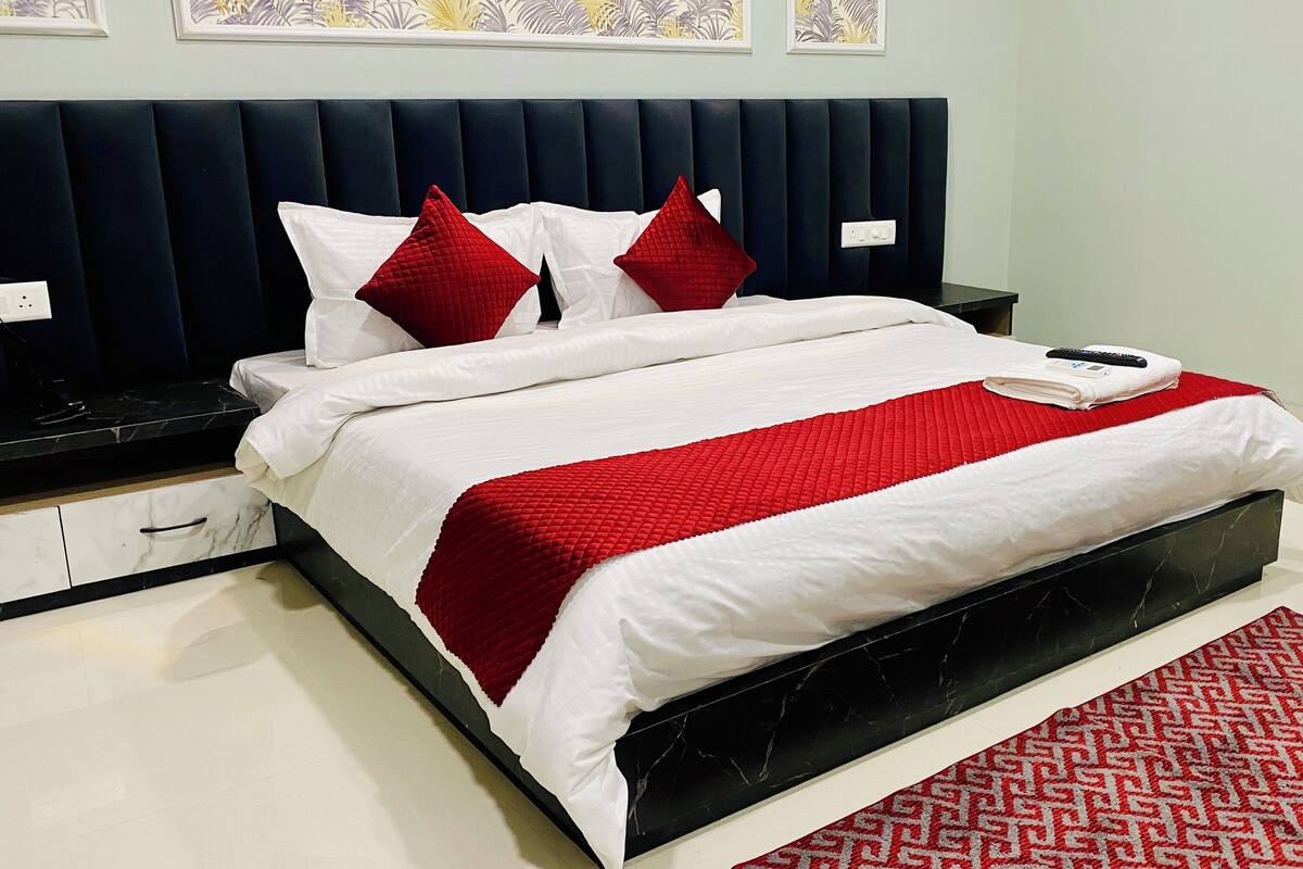A neatly made bed with white and red bedding, a black headboard, and a red patterned rug.
