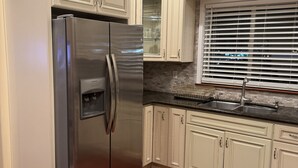 A kitchen with white cabinetry, a stainless steel refrigerator, a granite countertop, and a window with blinds. - Occidental college (Los Angeles)