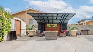 A covered outdoor seating area with wicker furniture, a potted plant, and a view of a house in the background. - Occidental college (Los Angeles)