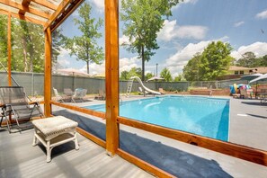A swimming pool with a slide, surrounded by lounge chairs and umbrellas, under a wooden pergola.