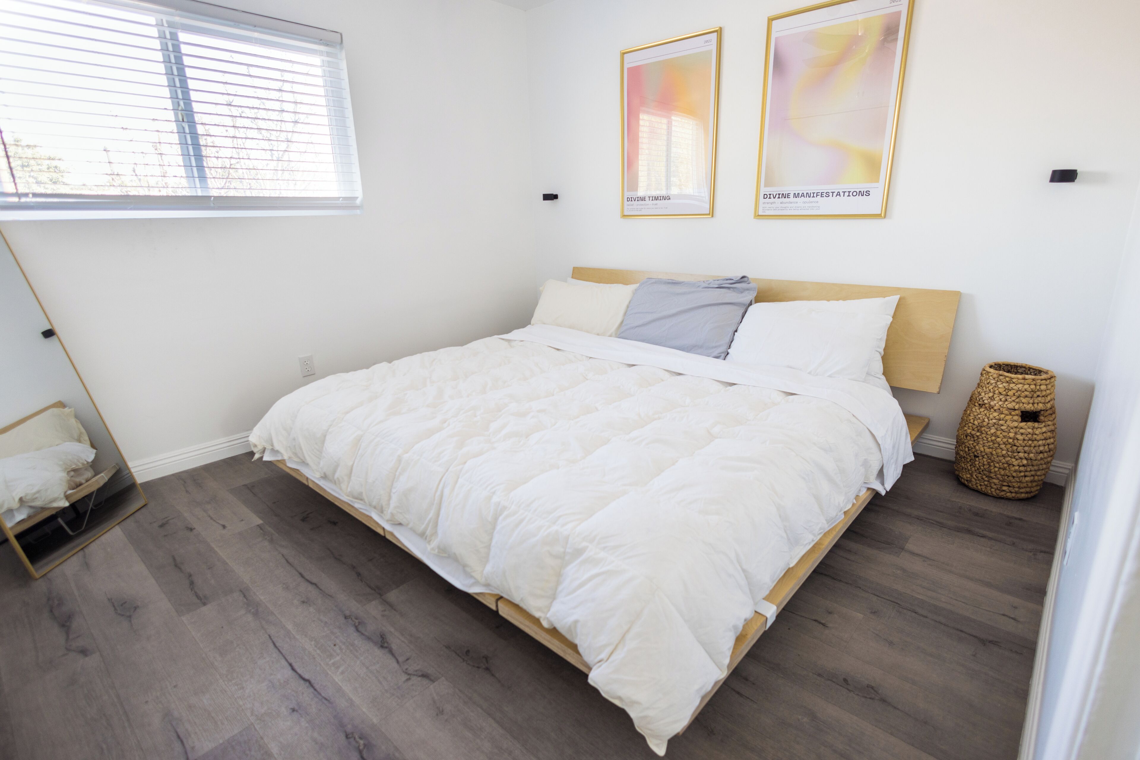 A bedroom with a large bed, a window with blinds, and two framed pictures on the wall.