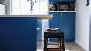 Une cuisine moderne avec des meubles bleus, un tabouret en bois et une fenêtre avec des stores.