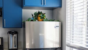 Une cuisine avec des meubles de couleur bleue, un réfrigérateur en acier inoxydable et une fenêtre équipée de stores.