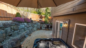 Un jacuzzi en un espacio exterior cubierto con pared de piedra, cerca de una valla de madera y mobiliario exterior.