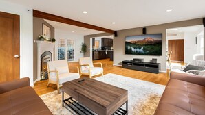 Un salón espacioso con chimenea, asientos cómodos, un televisor de pantalla plana y una cocina al fondo.