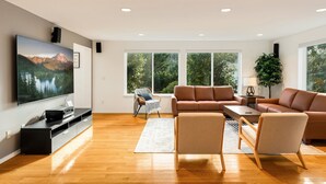 Una sala moderna con un televisor de pantalla plana, sofás de cuero, una mesa de centro y un ventanal con vistas a árboles.