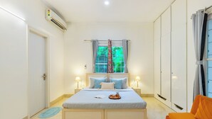 Un dormitorio con cama, lámparas de noche, ventana con cortinas, armario y un pequeño sofá naranja.