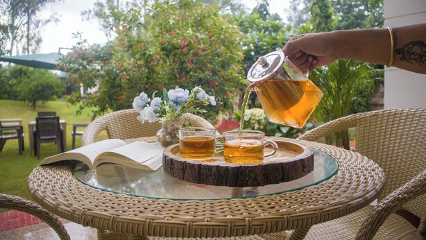Una mesita de mimbre con superficie de vidrio, dos tazas de té y un libro abierto.