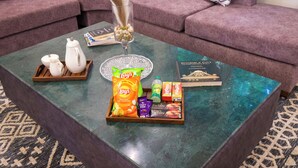 Una sala de estar con una mesa de centro de vidrio que muestra aperitivos, un libro y un jarrón decorativo.