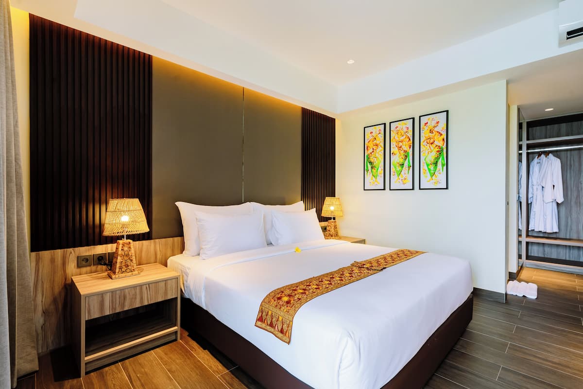 A hotel room with a large bed, two bedside tables with lamps, a wardrobe, and three framed artworks on the wall.