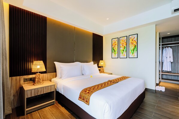 Une chambre d’hôtel avec un grand lit, deux tables de chevet avec des lampes, une armoire et trois œuvres d’art encadrées accrochées au mur.