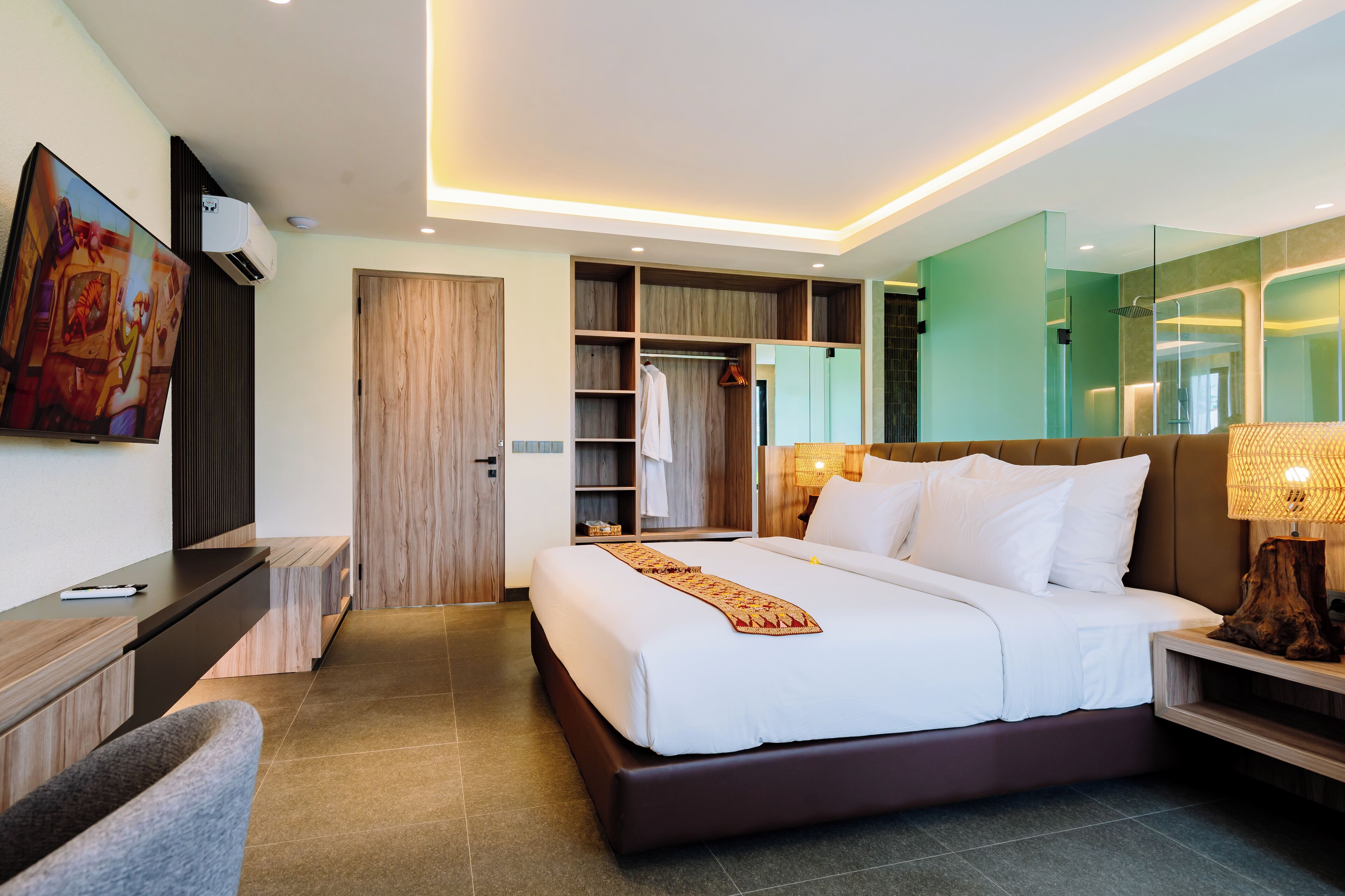 A modern hotel room with a large bed, a TV, a wardrobe, and a bathroom with a glass shower.