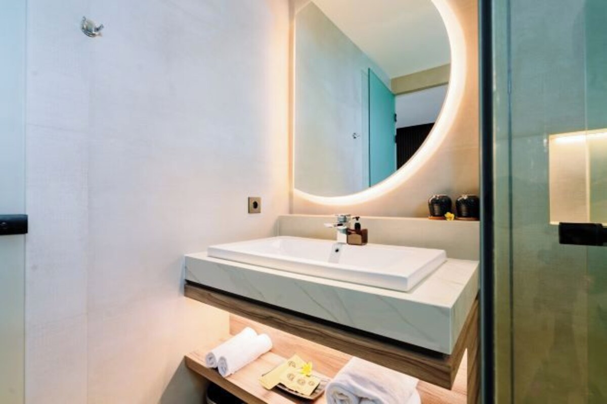 A modern bathroom with a large mirror, a white sink, and a wooden vanity.