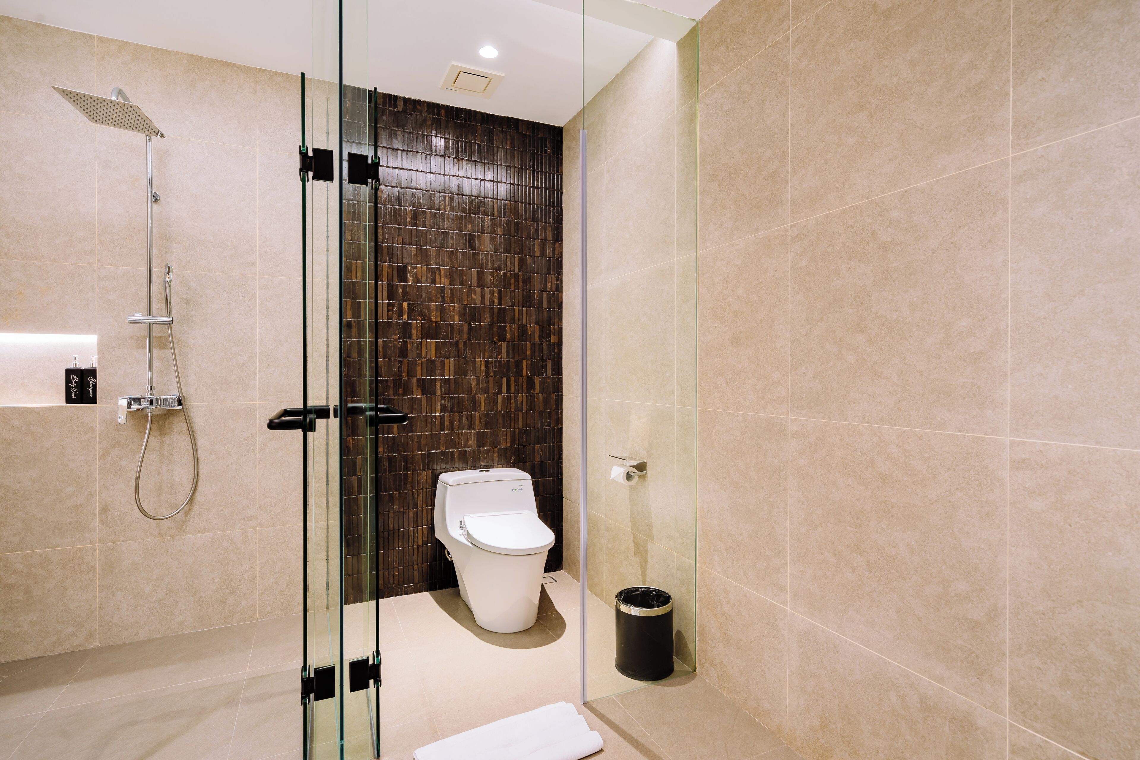 A modern bathroom with a glass-enclosed shower, a white toilet, and a trash can.