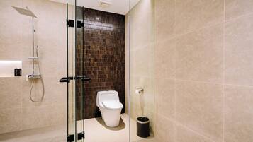 A modern bathroom with a glass-enclosed shower, a white toilet, and a trash can.