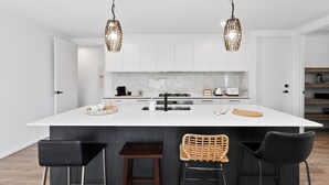 A modern kitchen with a central island, two hanging pendant lights, and four bar stools. - Adelphi Family Home Near Queenscliff Ferry 10 Min (Point Lonsdale)