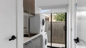 A narrow hallway with a washing machine, a sink, and wooden cabinets. - Adelphi Family Home Near Queenscliff Ferry 10 Min (Point Lonsdale)