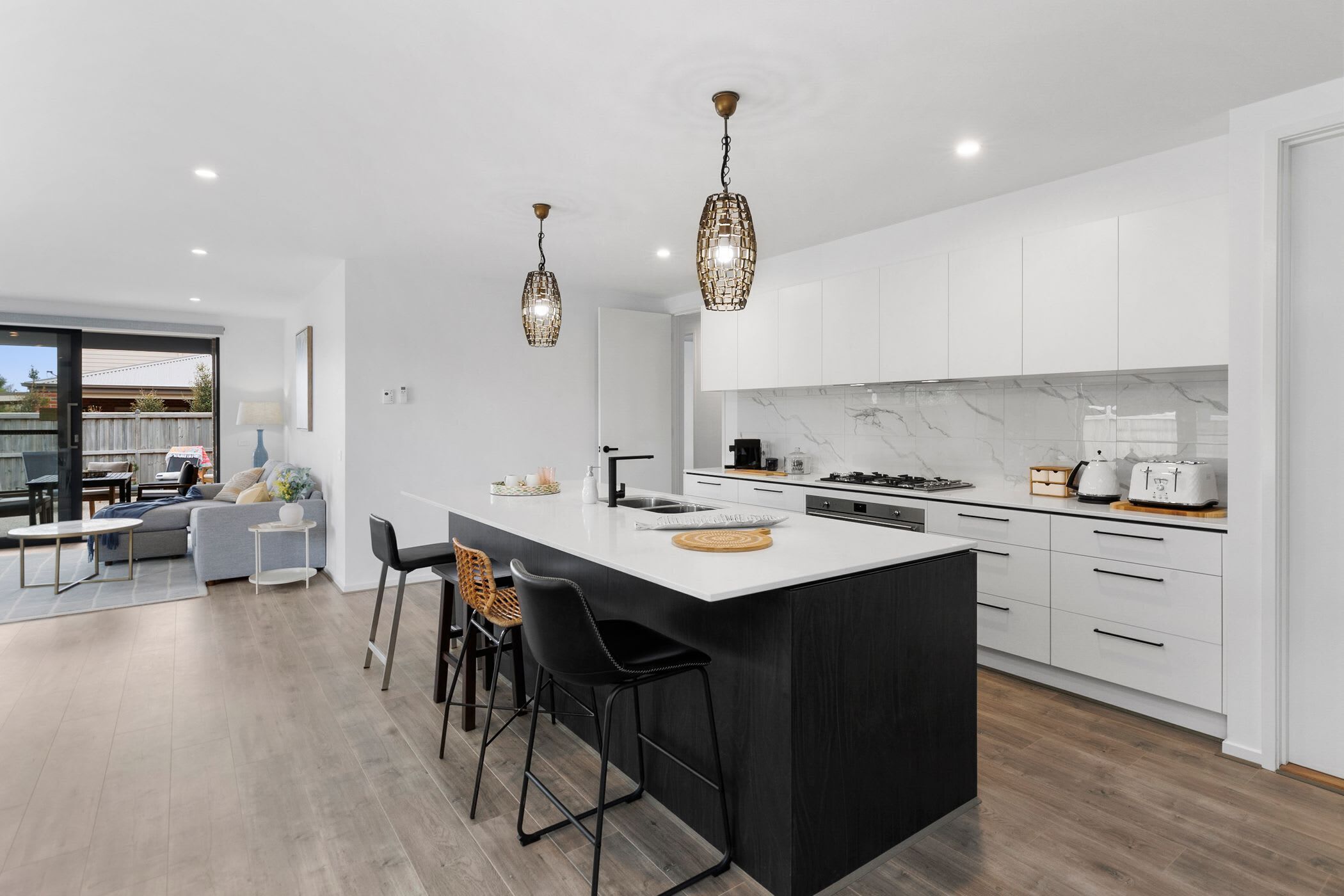 A modern kitchen with white cabinets, a marble backsplash, and a central island with bar stools.