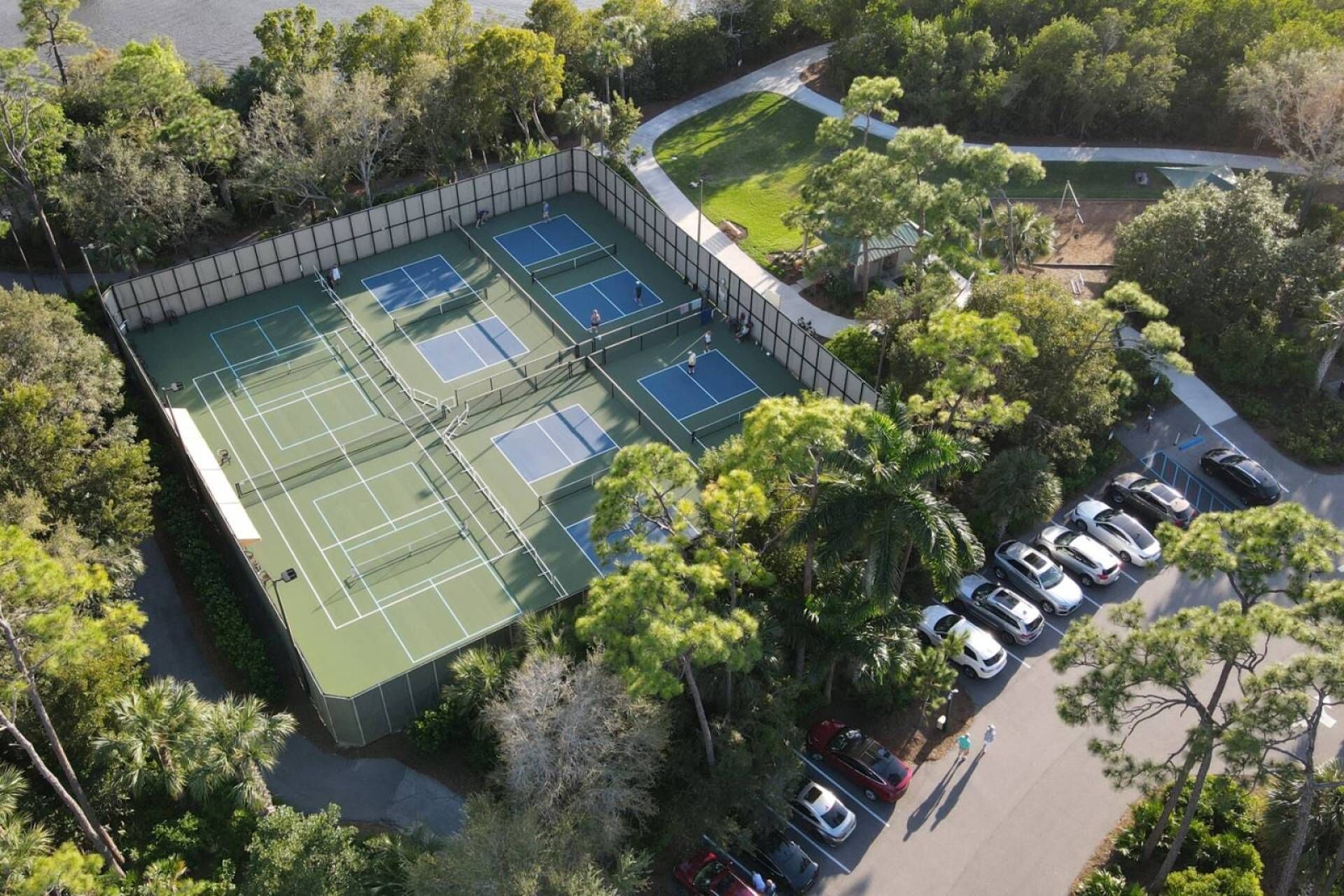 Een tenniscomplex omringd door bomen en een parkeerplaats met meerdere auto's.