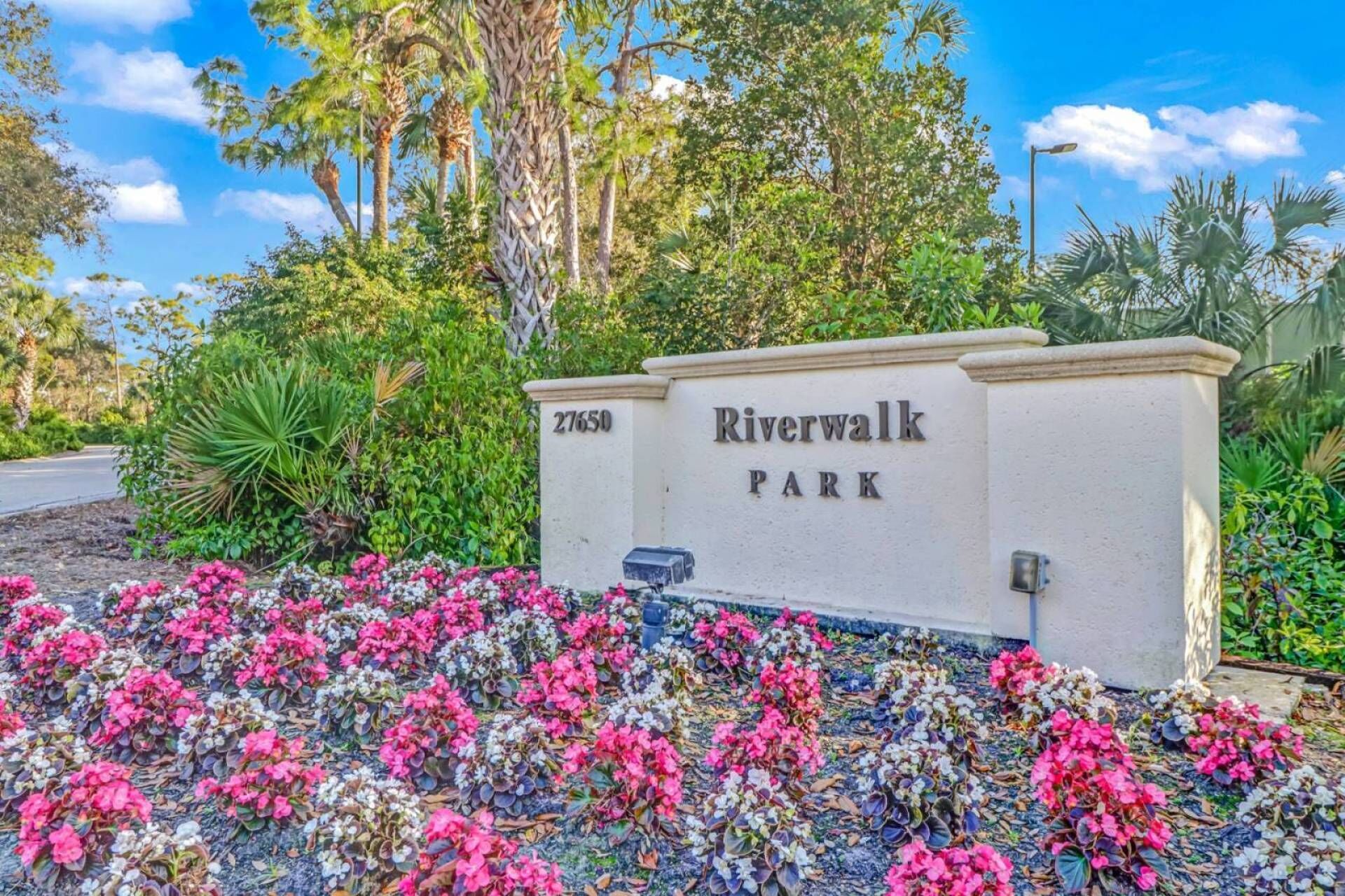 A sign for Riverwalk Park with a number 27650, surrounded by colorful flowers and greenery.