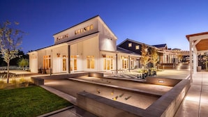 A modern building with a flat roof and large windows, surrounded by a well-lit courtyard with a pool and outdoor seating area.