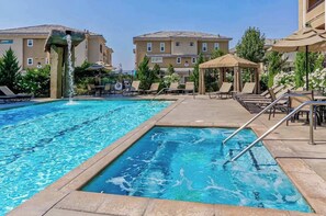 A swimming pool with lounge chairs and umbrellas, surrounded by buildings. - South Reno 1BR · Hot Tub, Mountain Views & Pool (Reno)